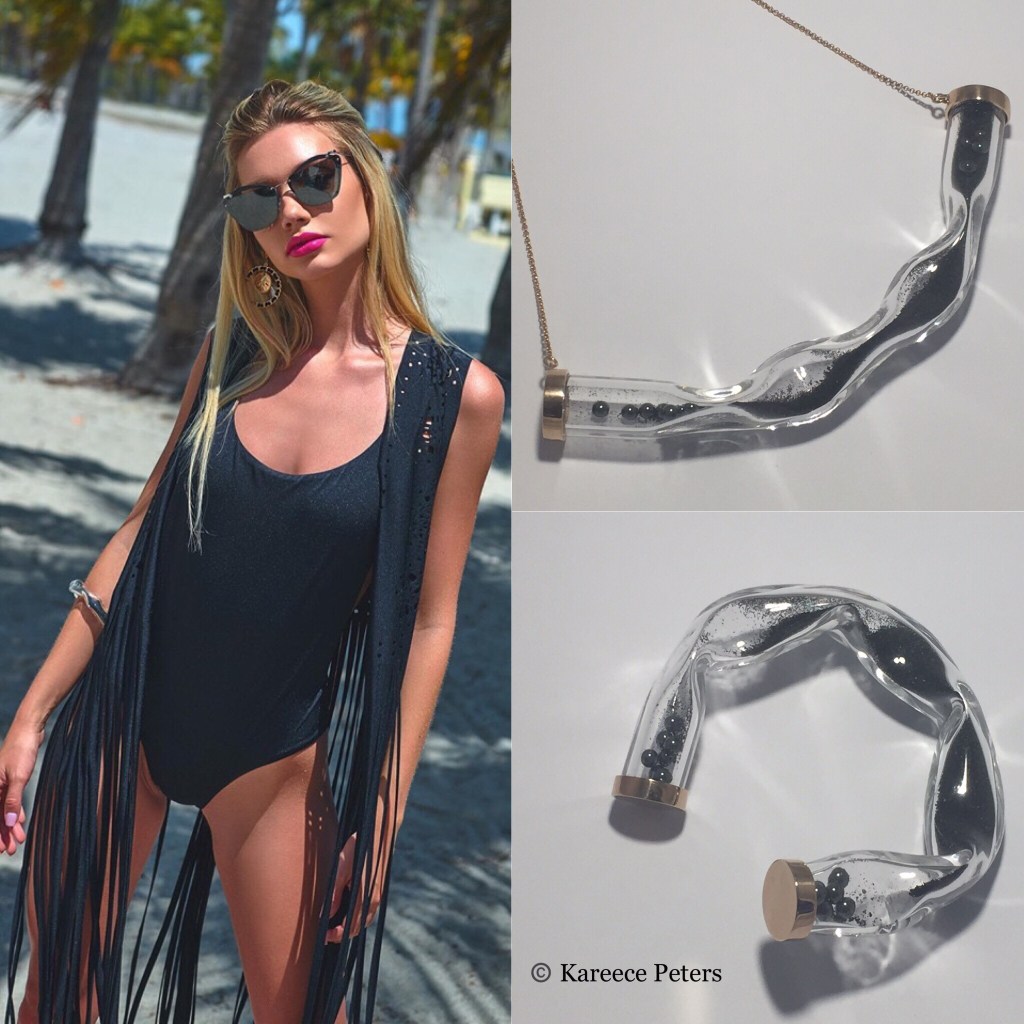 Blond haired model with sunglasses stands wearing a black swimsuit, and black bangle 